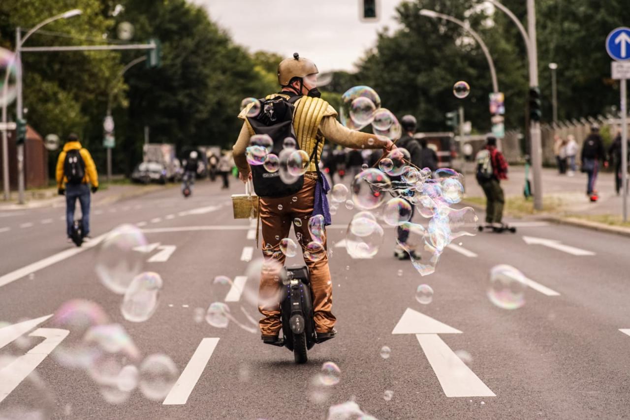 Mr.Pi, ein golden gekleideter Einradfahrer mit hunderten von Seifenblasen mitten auf einer breiten Straße im urbanen Raum.