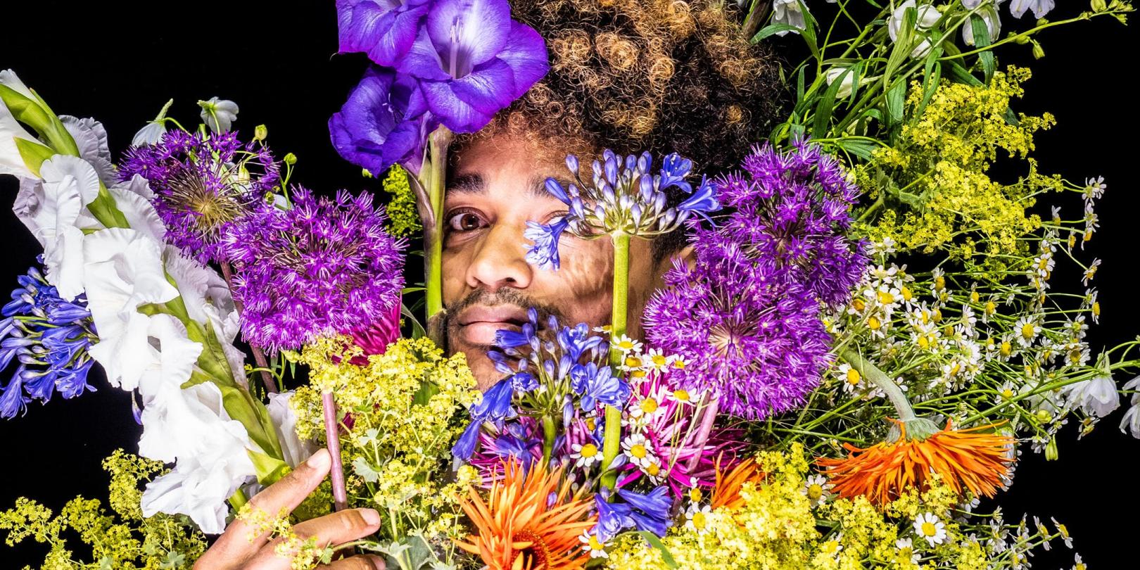 Ein Mann schaut hinter einem Strauß bunter Blumen hervor.