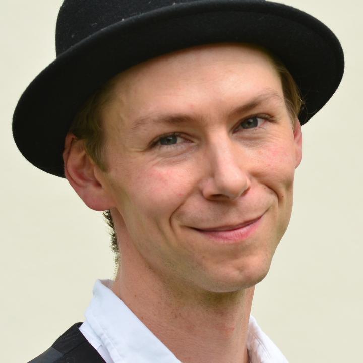 Portraitfoto eines freundlich Lächelnden jungen Mannes mit einem schwarzen Hut auf dem Kopf